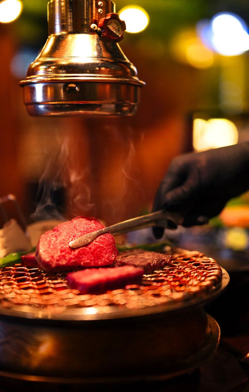 Hanwoo on a grill with smoke rising under a copper hood