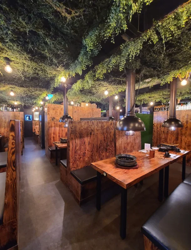 Booths of scorched wood under a vine-covered ceiling and string lights